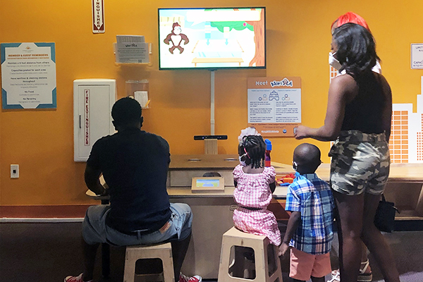 A family sits and stands in front of a an exhibit in a museum exhibit.