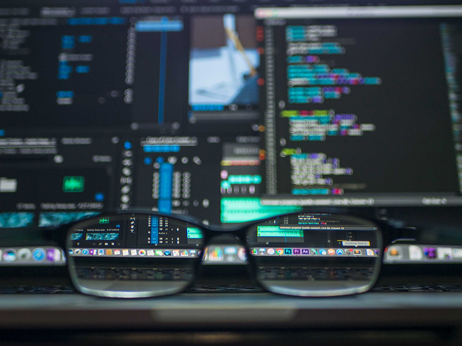 A stock image depicts reading glasses in the foreground with a blurred computer screen in the background. Portions of the screen visible through the lenses are in focus.