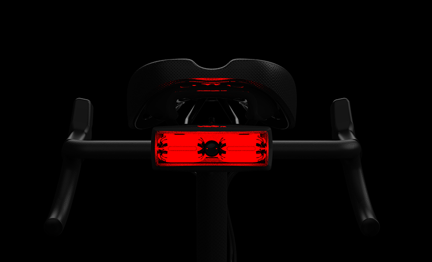 A light attached to the rear of a bike seat is lit up and red against a black background.