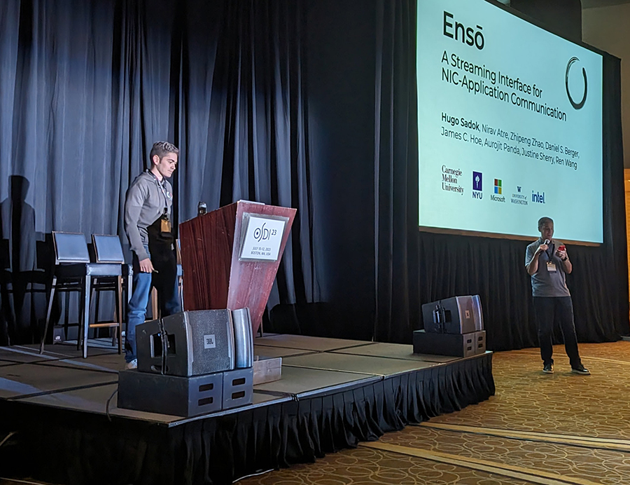A man stands behind a podium on a stage, while a screen on his left shows a presentation titled Enso, A Streaming Interface for NIC-Application Communication.