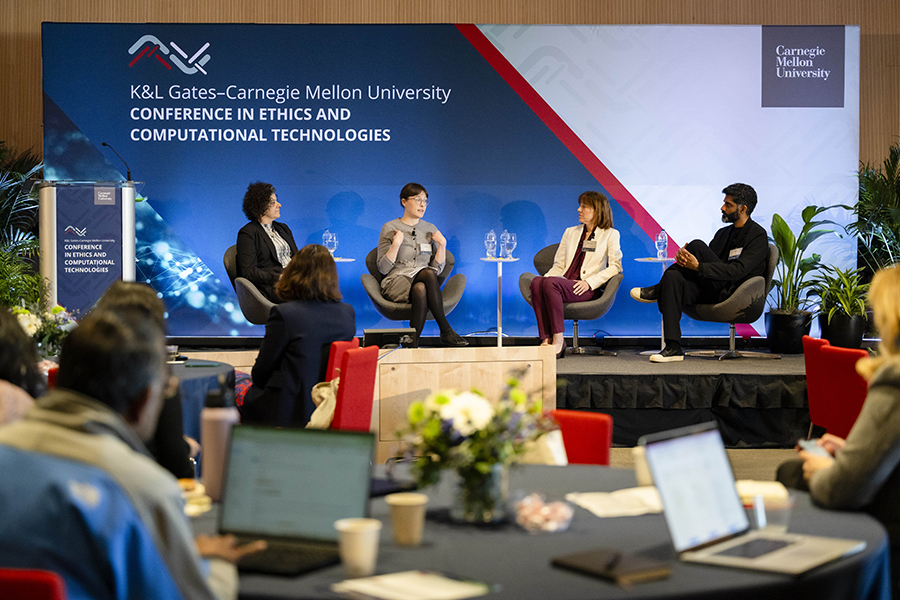  Three woman and a man sit on a stage in front of a sign promoting the K&L Gates Conference in Ethics and Computational Technologies.