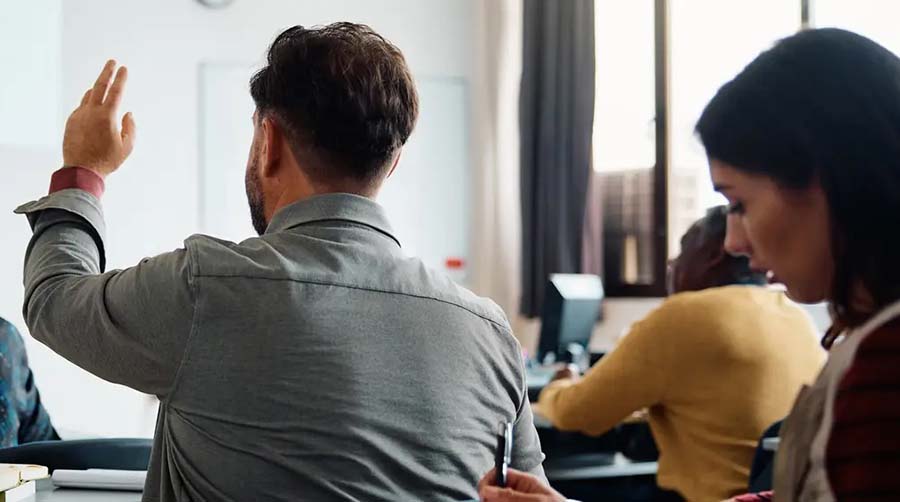  A man in a classroom raises his hand.