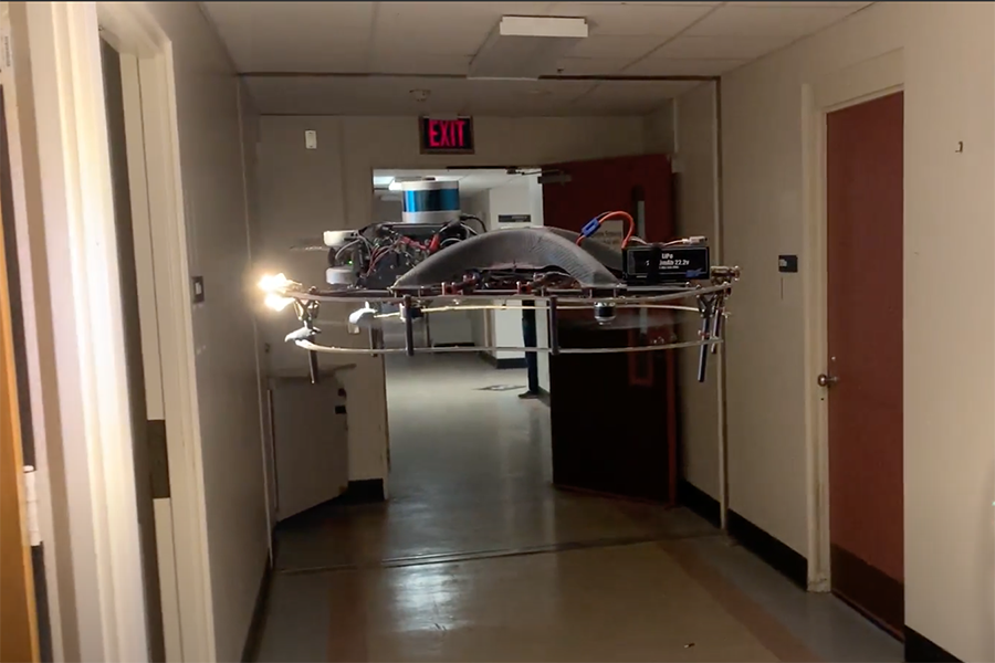  A robotic drone hovers in midair in a corridor, its headlight focused on a doorway.