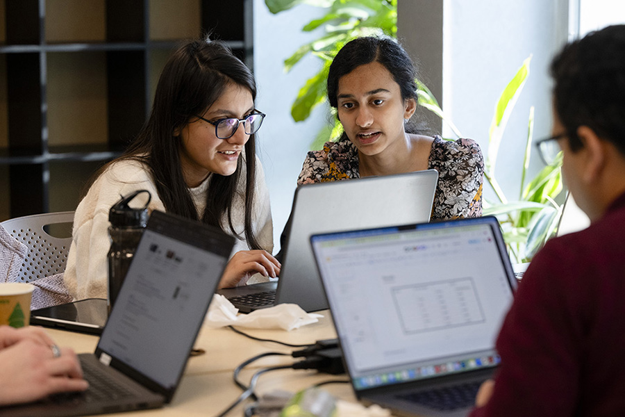  Two women work on a laptop in front of a window.