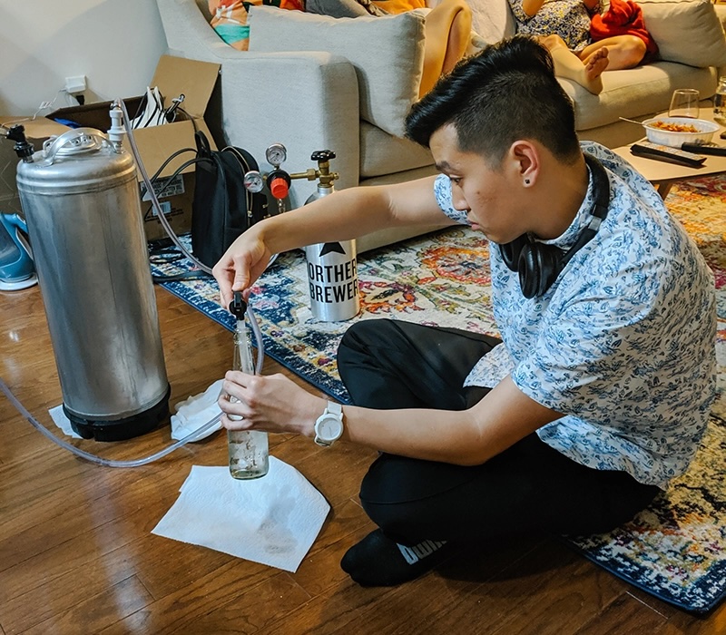  A man with headphones around his neck sits on the floor, filling a bottle from a tank.