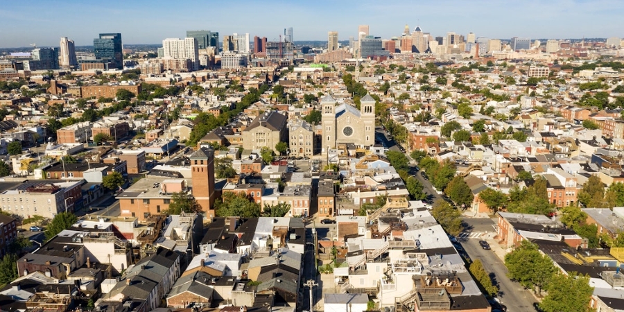 A decorative aerial photo of Baltimore shows its many row homes against a blue sky. A church is in the center of the photo.
