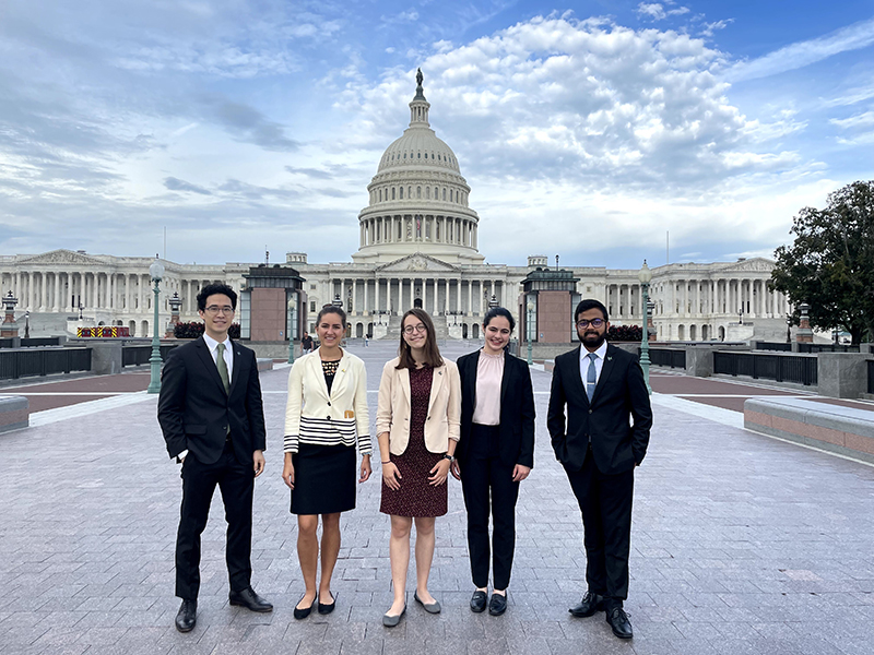 Five students — a male, three females and another male — pose in front of the U.S. Capitol.