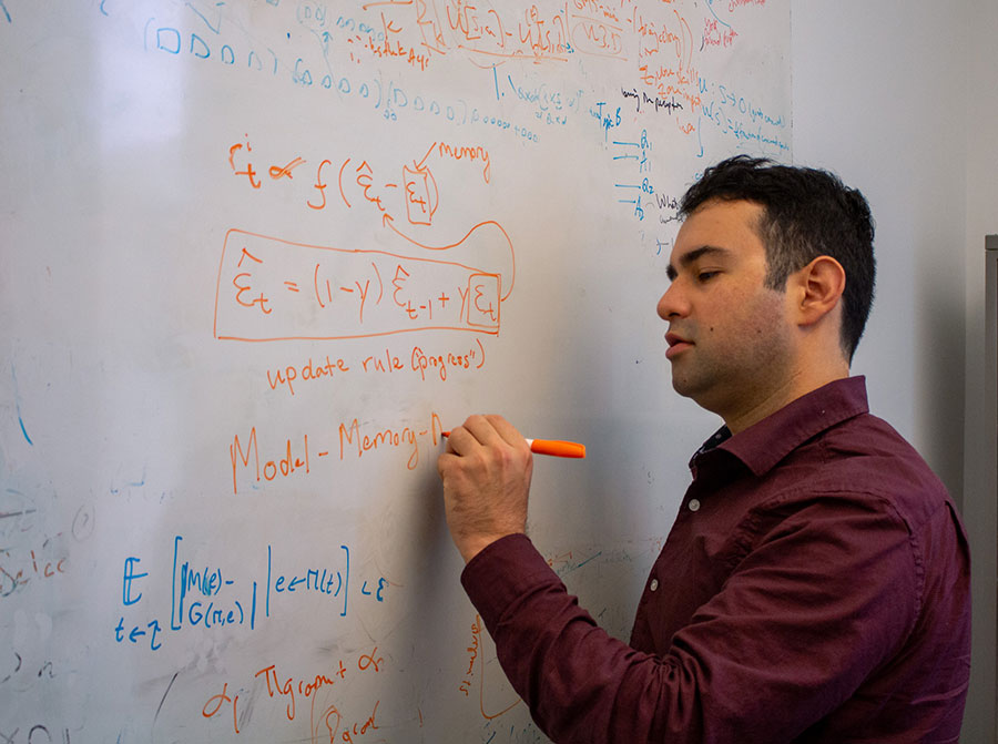  A man writes a formula in orange marker on a dry erase board.