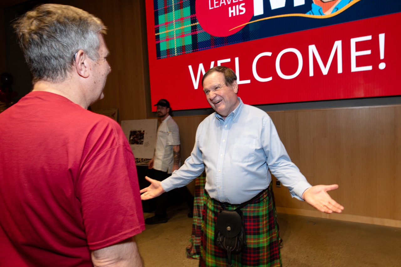 A man with outstreched arms smiles in greeting to a man approaching him