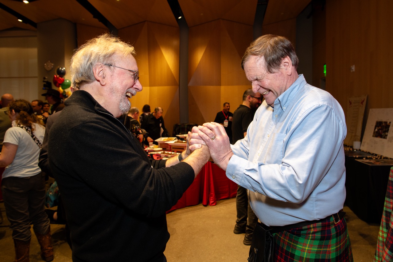 Two men clasp hands and smile at a retirement celebration