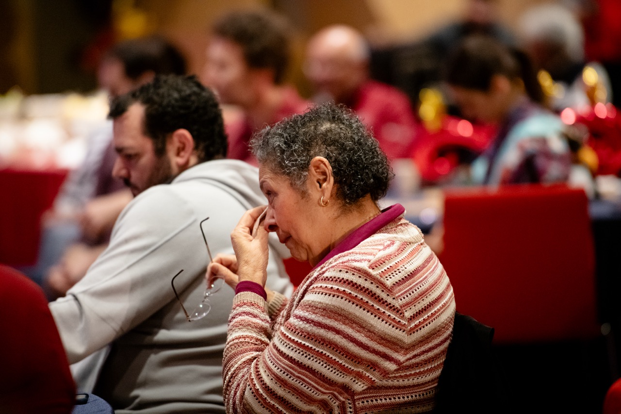 A woman holds her glasses in front of her while wiping tears from her eyes during remarks